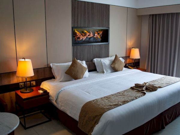 A hotel room with a large bed, decorative pillows, bedside lamps, and a modern wall art piece above the headboard is displayed.