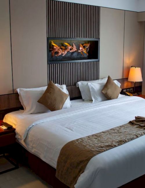 A neatly made hotel room features a large bed with pillows, bedside tables with lamps, and curtains by the window, creating a cozy ambiance.