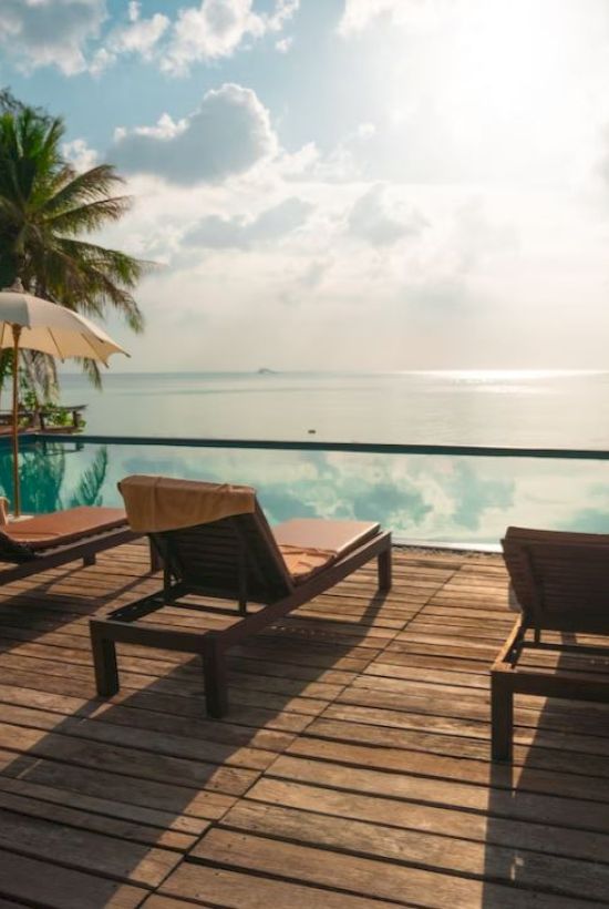 A tranquil poolside scene with loungers, parasols, and a view of the ocean under a partly cloudy sky creating a serene atmosphere.