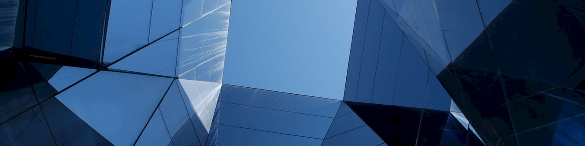 A modern architectural structure with angular, reflective surfaces forms a geometric pattern against the sky.