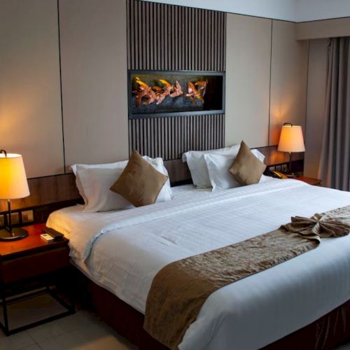 A neatly arranged hotel room features a king-sized bed, bedside lamps, and decorative pillows, creating a cozy and inviting atmosphere.