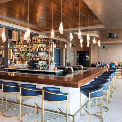 A modern bar interior with sleek seating, hanging lights, and a well-stocked bar area in an open, stylish setting.