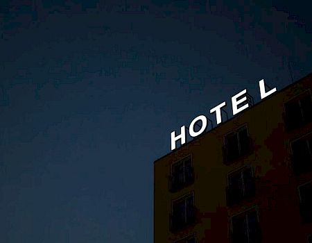 The image shows the facade of a building at night with the word "HOTEL" illuminated in white letters at the top.