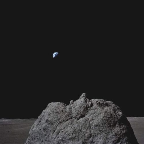 A rocky surface and mound in the foreground; Earth is visible in the distant dark sky, appearing small and circular.