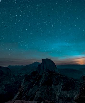 A night scene with a clear starry sky over a mountainous landscape, and a subtle glow on the horizon.
