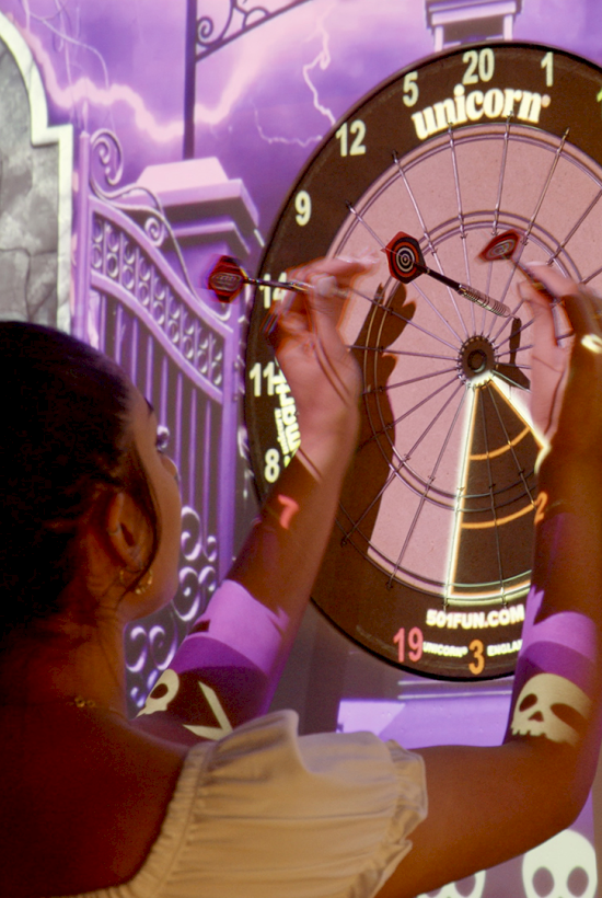 A person interacts with a projected game, adjusting dials on a clock with names and scores on the side.