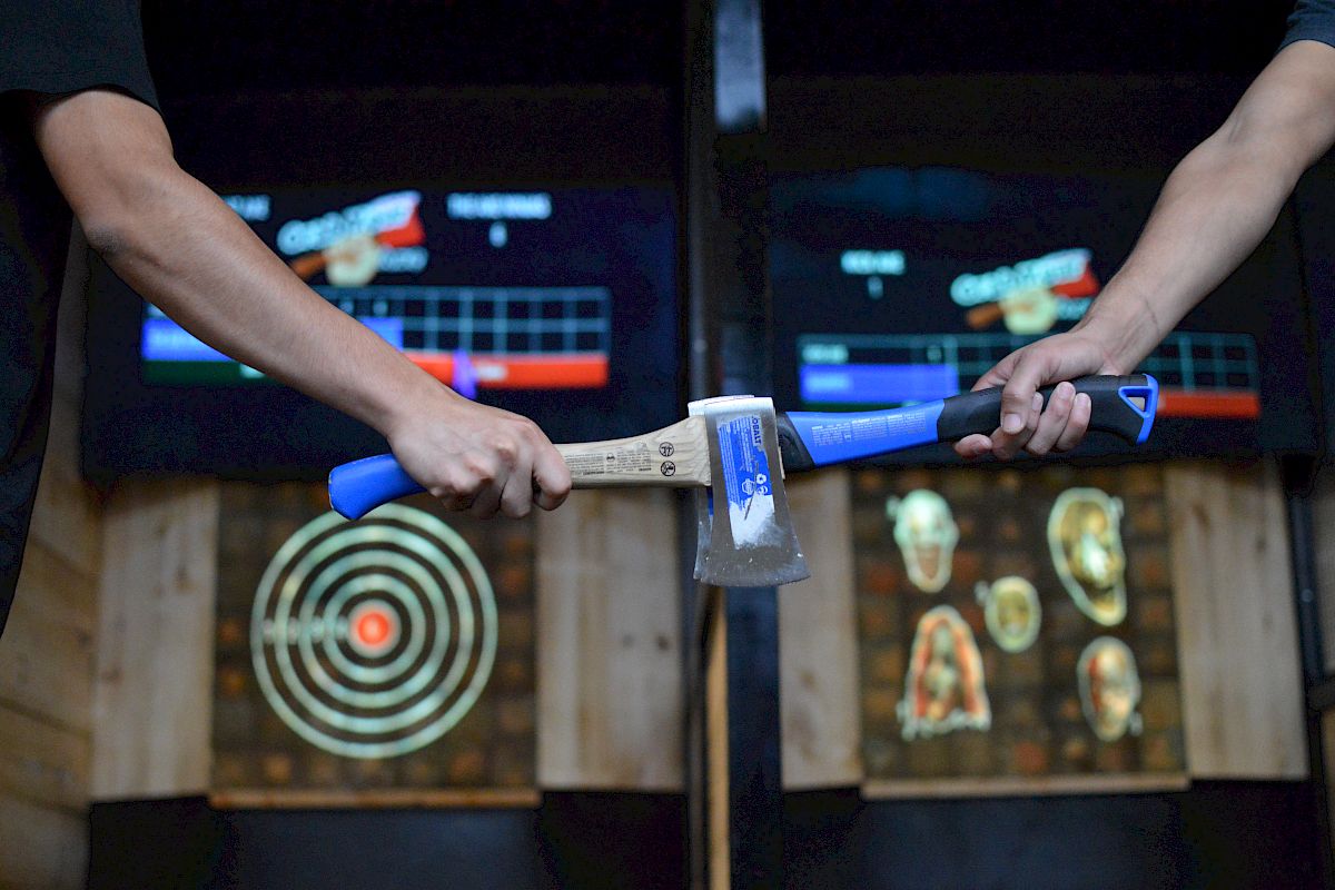 Two people holding axes in front of electronic target boards in an axe-throwing venue.