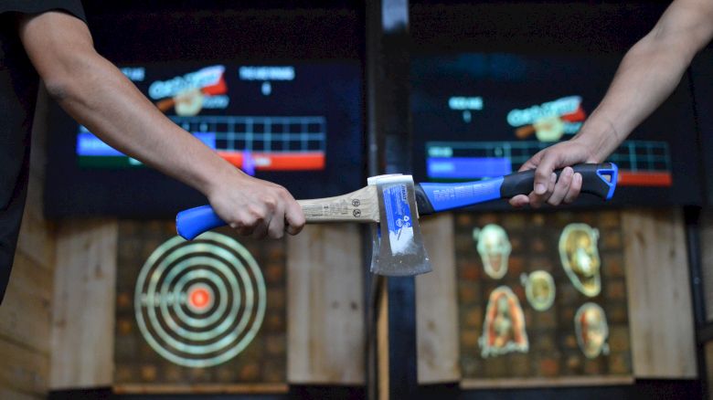 Two people holding axes in front of electronic target boards in an axe-throwing venue.