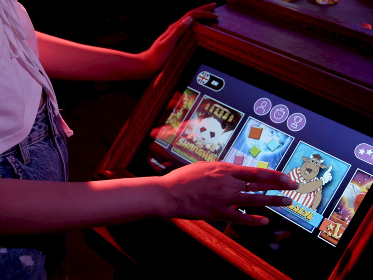 A person is using a touchscreen slot machine with various symbols and games displayed.