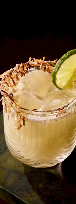 A salted, lime-garnished cocktail with ice and a sugar-rimmed glass, topped with a lime wedge and a slice of cucumber perhaps.