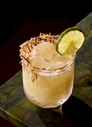 A tropical cocktail on ice with a lime wedge garnish, served in a short glass. Top it at 140 characters, always ending the sentence.