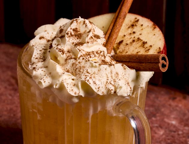A frosty beer mug with a big foamy head, a cookie and a straw perched on the rim, and a dark background.