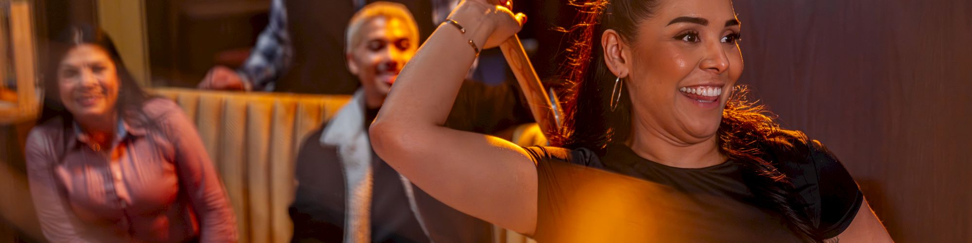 A woman in the foreground twirls her hair and smiles confidently, while three people lounge in the background of a cozy, dimly lit room.
