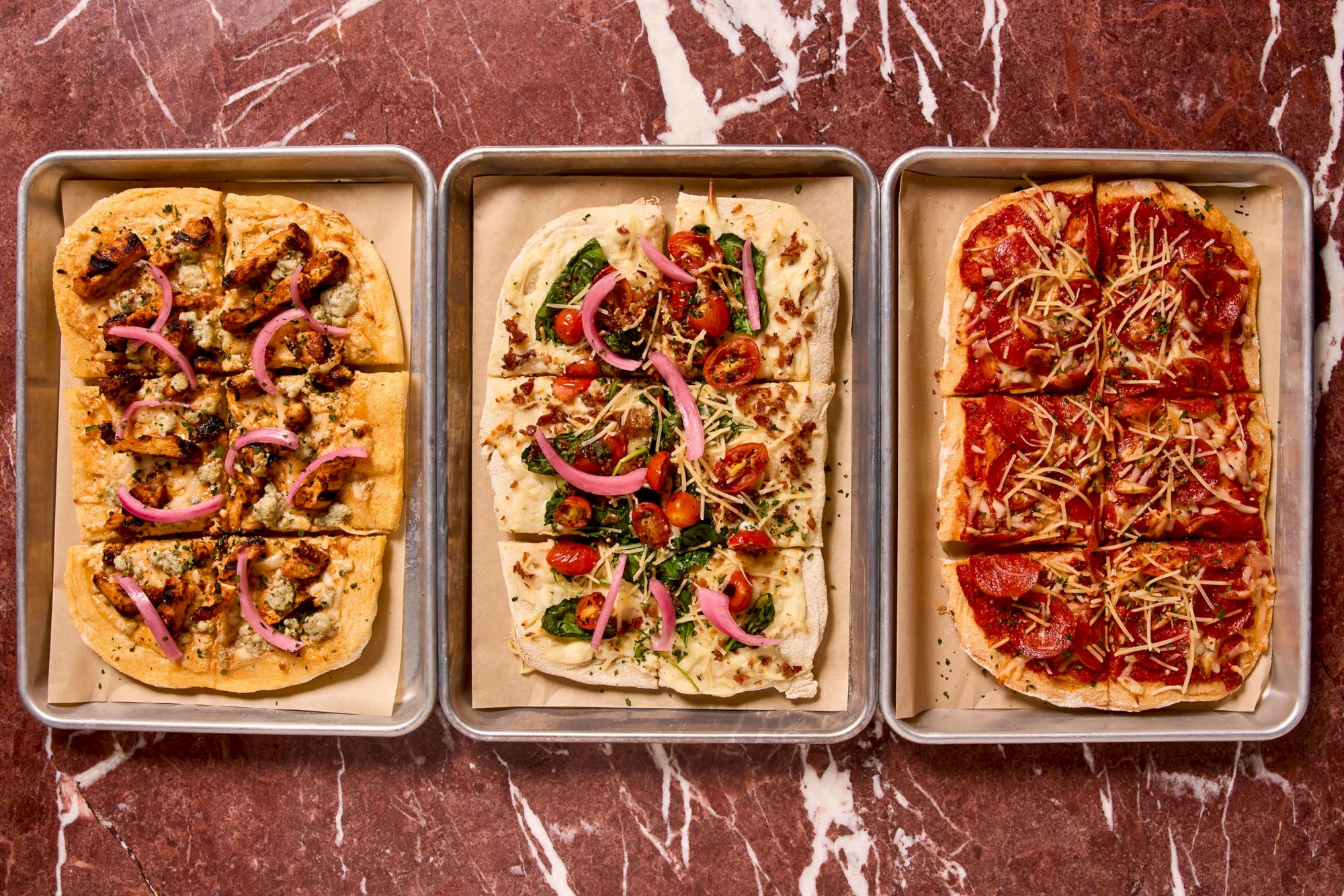 Three pizzas on baking trays with toppings: left looks like mushrooms and onions, middle has greens and peppers, right appears pepperoni with cheese. But the prompt asks to end the sentence with a period and 140 chars max. Ensure 140 chars and ends with a period.