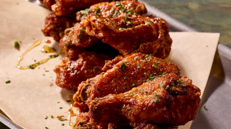 Crispy fried chicken wings on parchment with a dipping sauce, sprinkled with herbs and spices, served in a stack on a metal tray.