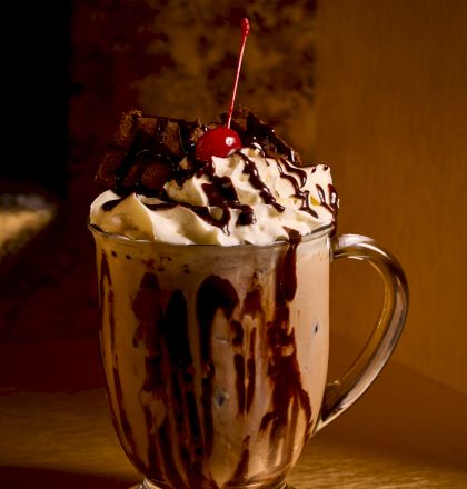 A chocolate dessert beverage with whipped cream and a sprinkle of cacao on top in a glass mug.