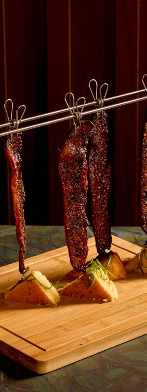 A wooden play gym with a small rope ladder and hanging fabric dolls/figures wearing patterned clothing, standing on a bright yellow floor mat.