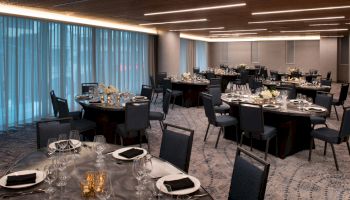 The image shows an elegantly set dining area with round tables, neatly arranged chairs, and decorative tableware, ready for an event.