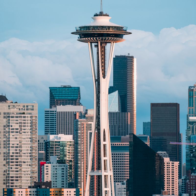 The image shows the Space Needle with a backdrop of modern skyscrapers and a cloudy sky.