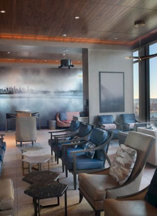 A modern lounge with stylish seating, large windows, and a panoramic view of a cityscape and water.