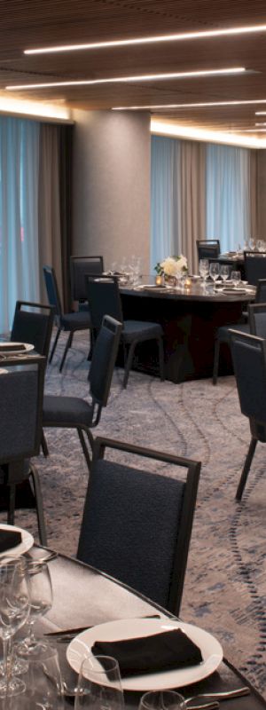 The image shows a banquet hall with round tables set for a formal event, featuring elegant table settings and dim ambient lighting.