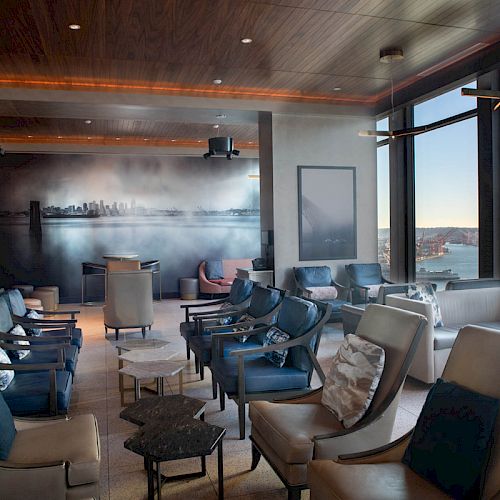 A stylish lounge with comfortable seating, large windows offering a scenic view, and a mural of a city skyline.