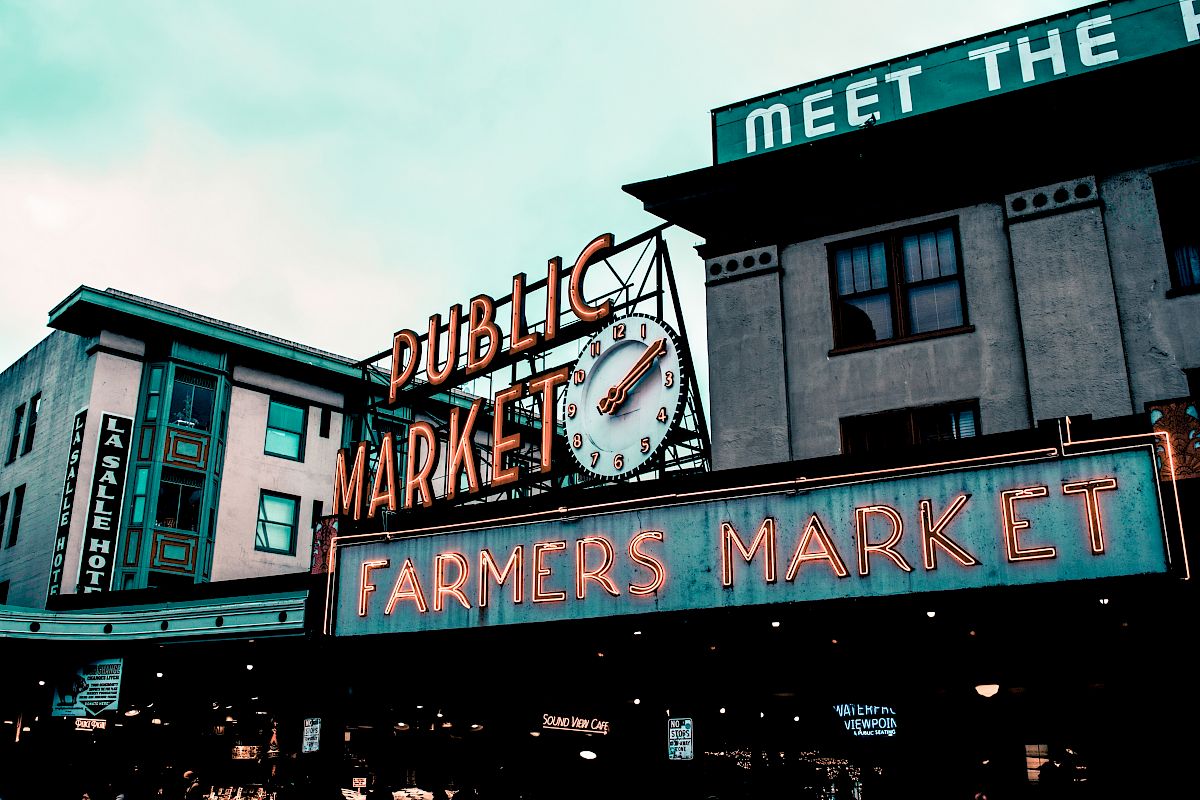 The image shows a famous public market sign with a clock, reading "Public Market" and "Farmers Market," with surrounding buildings.