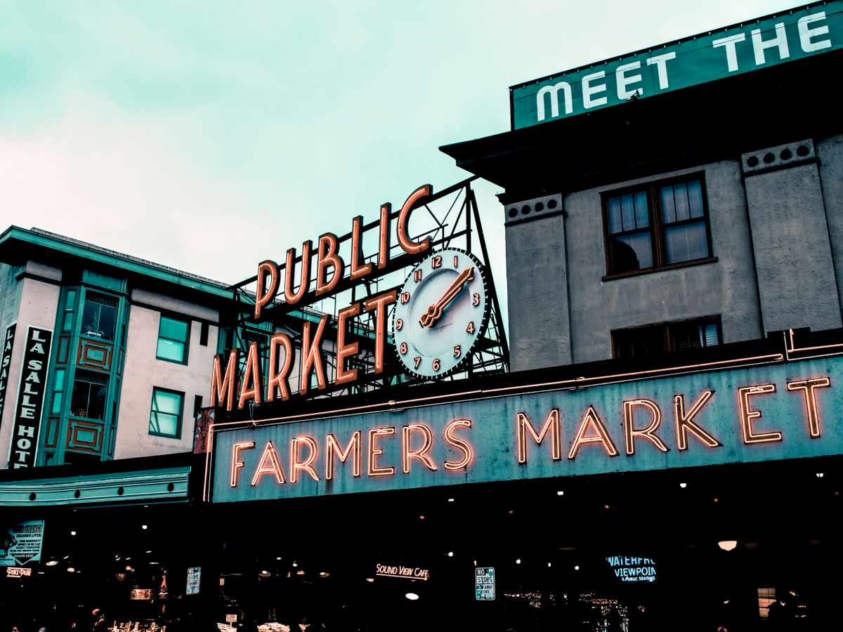 The image shows a famous public market sign with a clock, reading "Public Market" and "Farmers Market," with surrounding buildings.