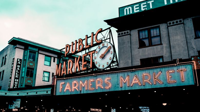 The image shows a famous public market sign with a clock, reading "Public Market" and "Farmers Market," with surrounding buildings.